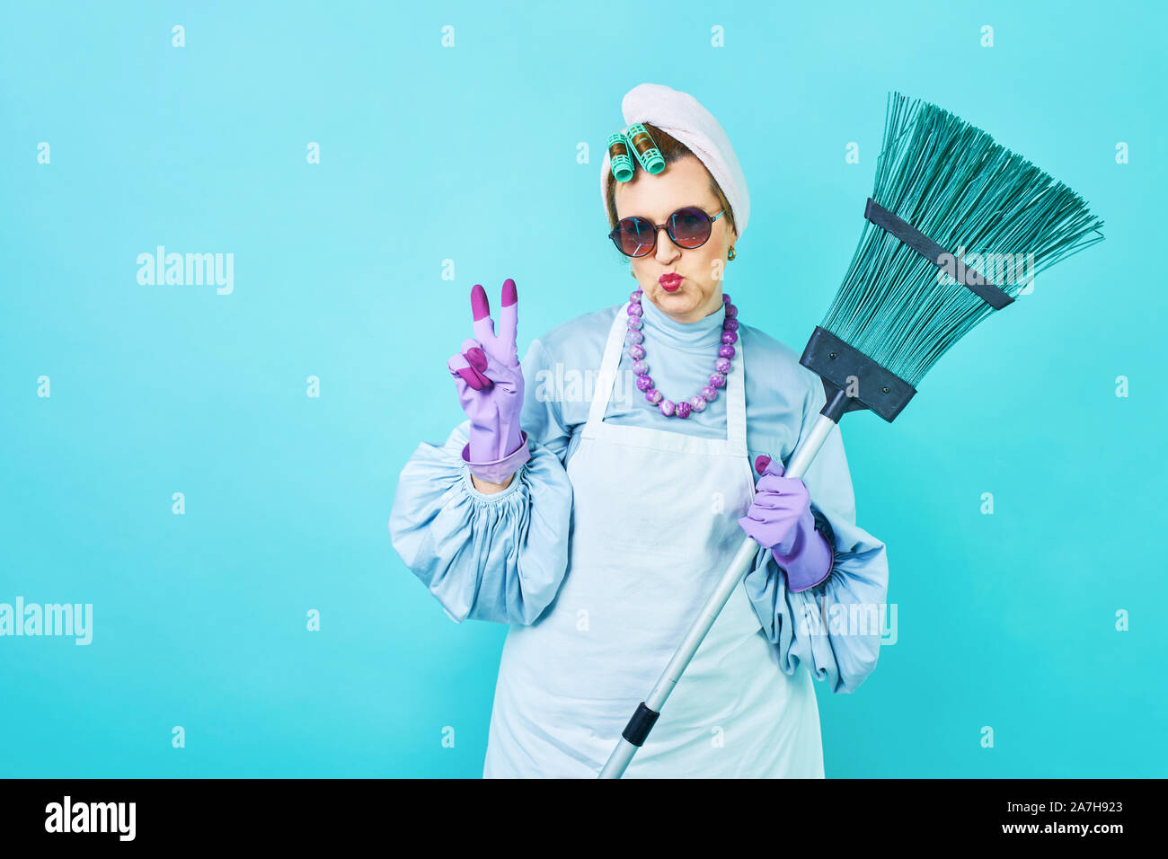 Donna delle pulizie divertente. Anziani funny casalinga ingannare circa con una scopa. Corpo pieno isolato blu. Pulizia comico lady, vecchia donna funky Foto Stock