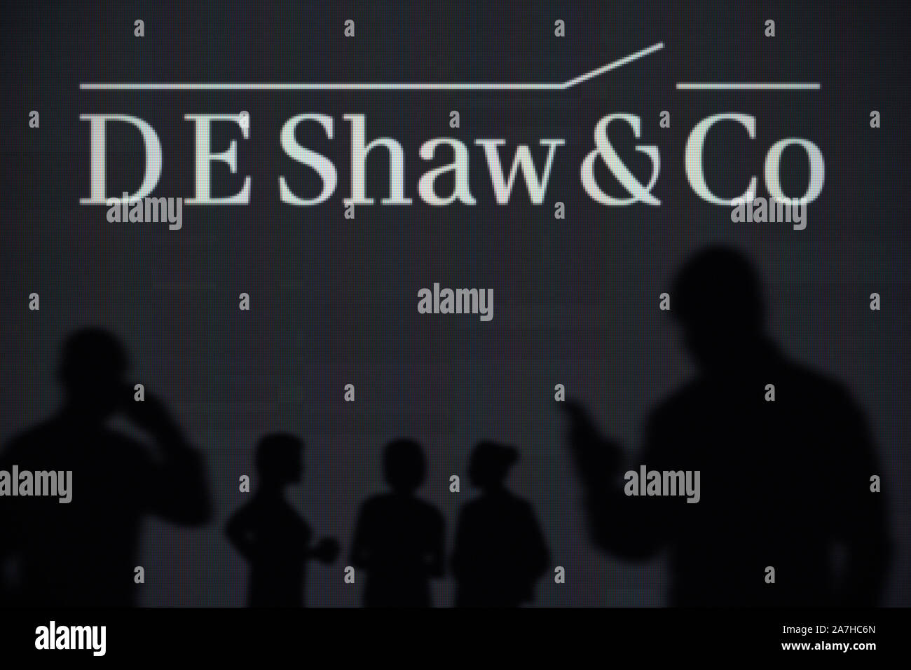 L D E Shaw Group logo è visibile su uno schermo a LED in background mentre si profila una persona utilizza uno smartphone (solo uso editoriale) Foto Stock