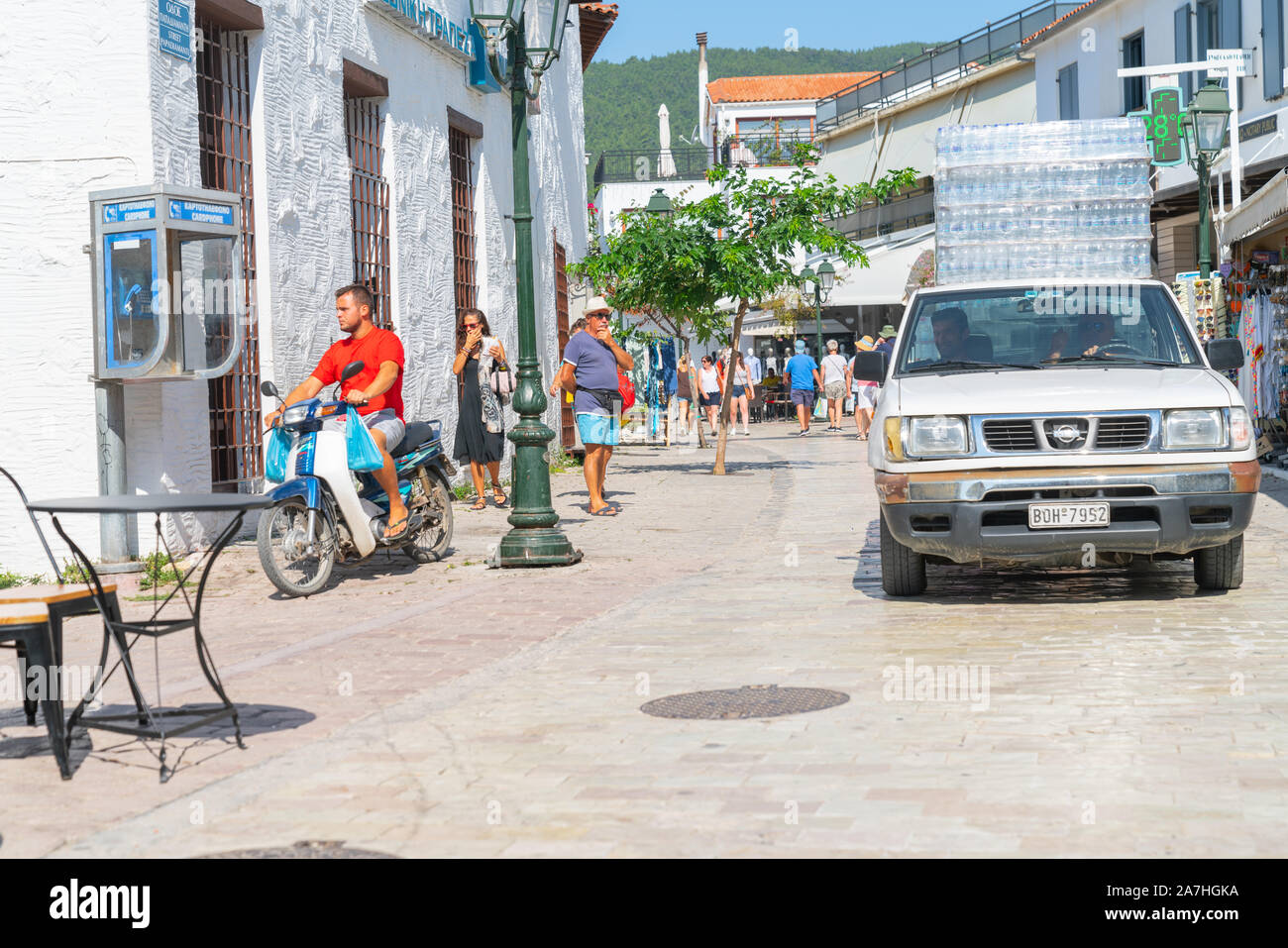 Skiathos Grecia - 4 agosto 2019; il carrello caricato con plastica bottiglie di acqua che viene erogata in strada con i turisti e il motociclista in tipico greco ISL Foto Stock