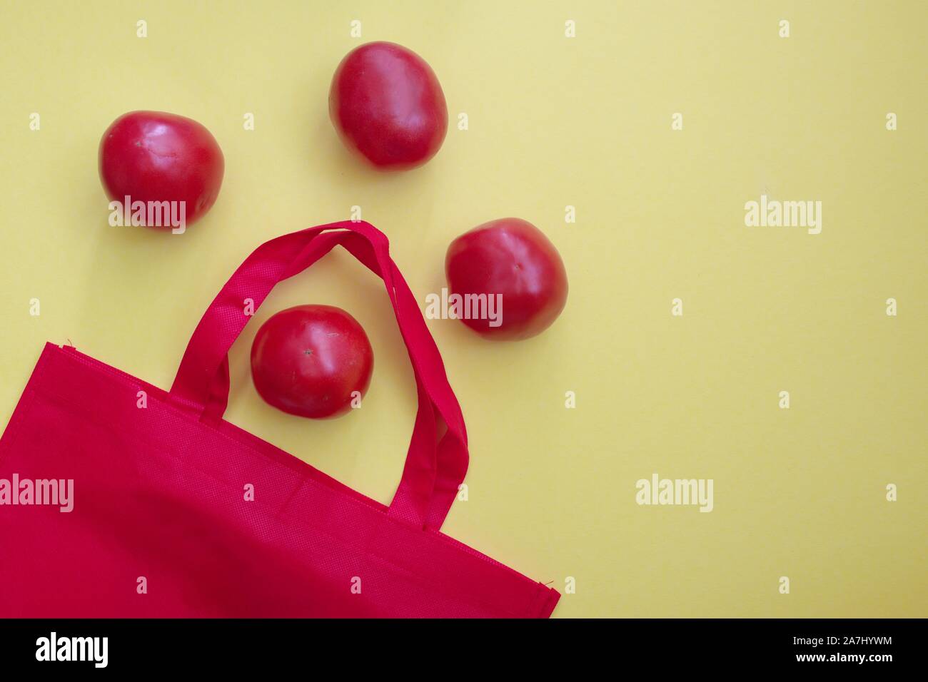 Riutilizzabili rosso shopping bag con pomodori contro lo sfondo giallo Foto Stock