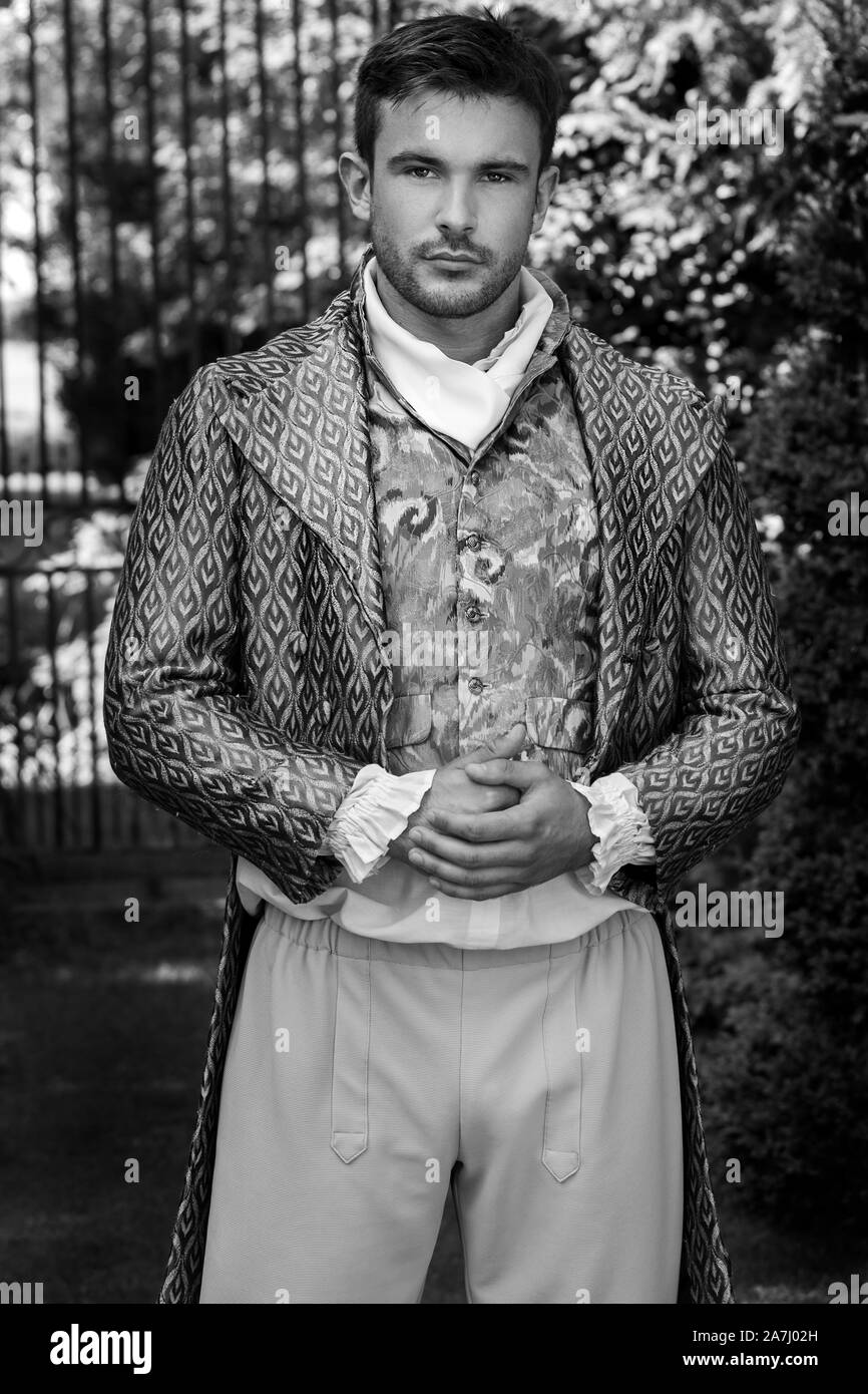 Ritratto di gentiluomo attraente vestito in costume d'epoca in piedi in dimora signorile cortile con ringhiere in background Foto Stock