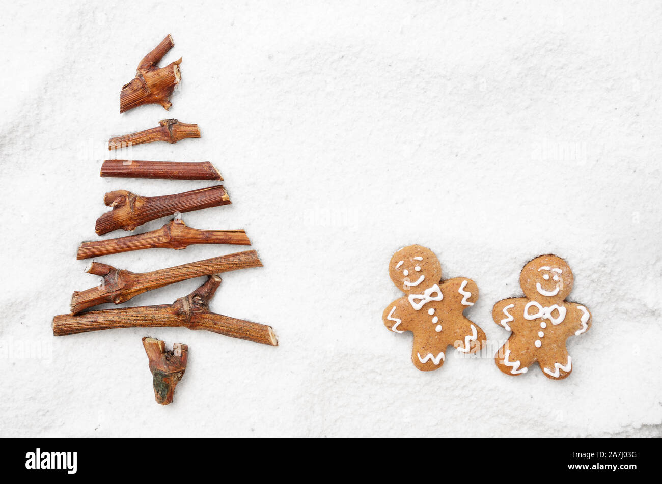 Piatto stilizzato laici albero di Natale fatto di piccoli ramoscelli e gingerbread man cookies sulla neve sullo sfondo. Spazio per il testo Foto Stock