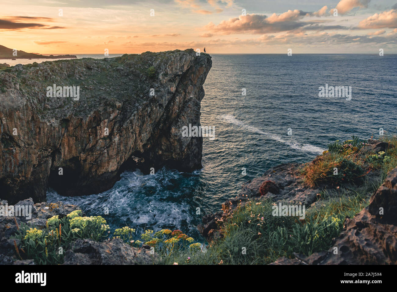 Paesaggio con la sagoma di un uomo in piedi sul bordo della scogliera sulla costa del mare del nord della Spagna, nelle Asturie e in Europa al tramonto colorato in estate Foto Stock