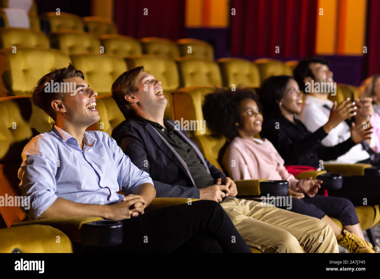 Ridendo casual uomini seduti su sedie morbido e ridere mentre si guarda divertente muoversi durante la showtime in movie theater Foto Stock
