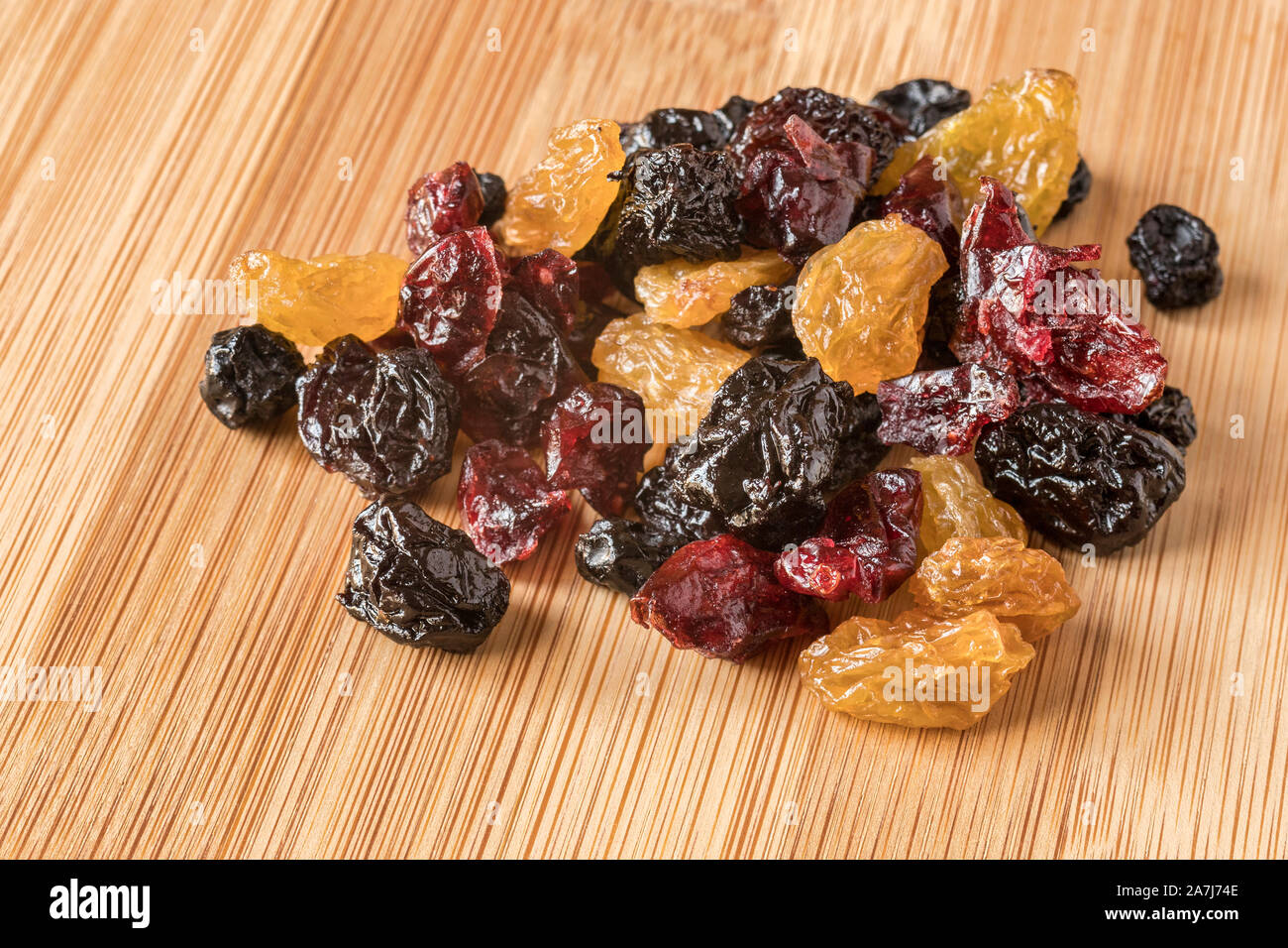 Una manciata di frutta secca mista, con uva passa dorata, ciliegie, mirtilli e mirtilli rossi, su una scheda di bambù. Foto Stock