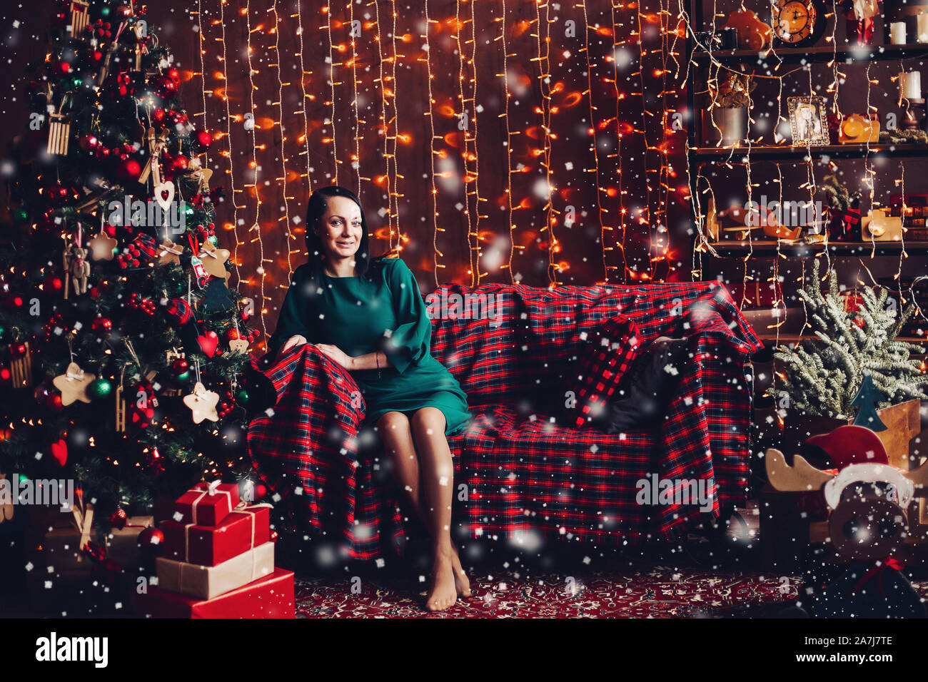 Donna sorridente in elegante abito verde sul lettino a albero di Natale. Foto Stock