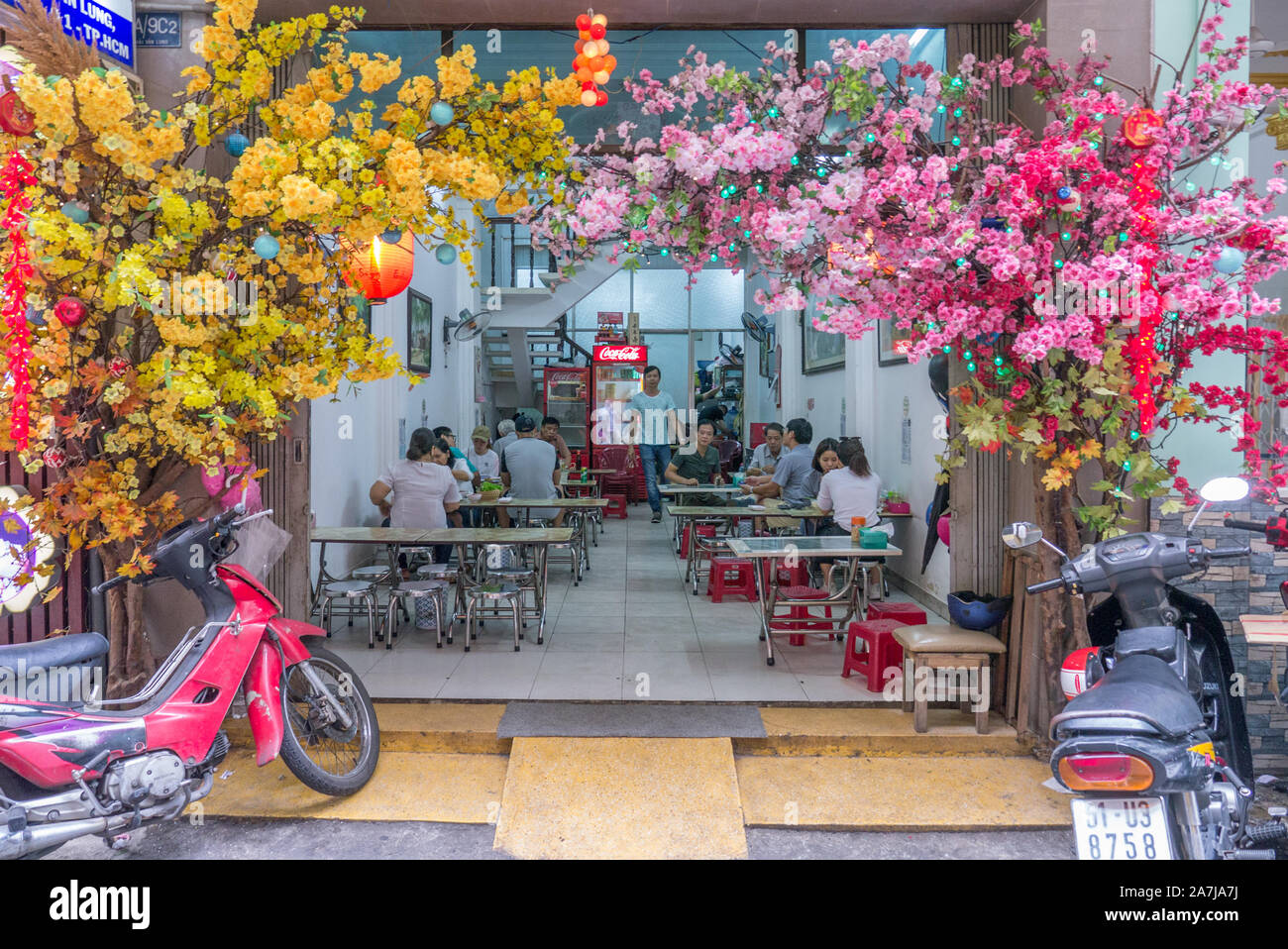 Ristorante giapponese situato in vicolo decorato con finti fiori di ciliegio giallo e rosso con scooter parcheggiati di fronte. Foto Stock