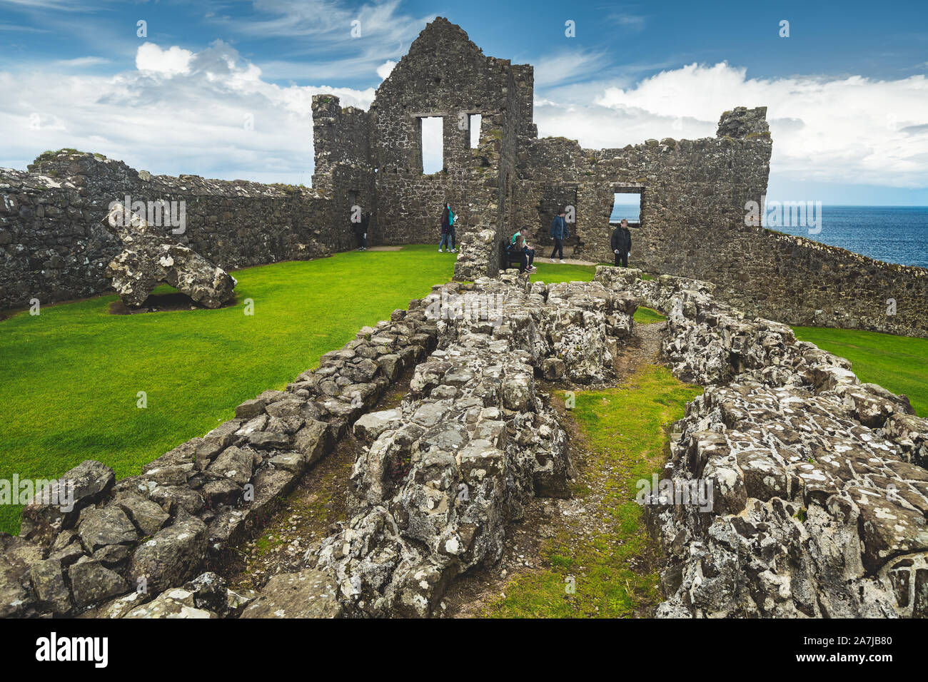 Ha rovinato il vecchio castello di Costa Irlanda del Nord. Pareti in rovina di edificio medievale, cielo blu con nuvole e mare sullo sfondo. I turisti che visitano un paesaggio fantastico con rimangono di antica casa a Costa Foto Stock