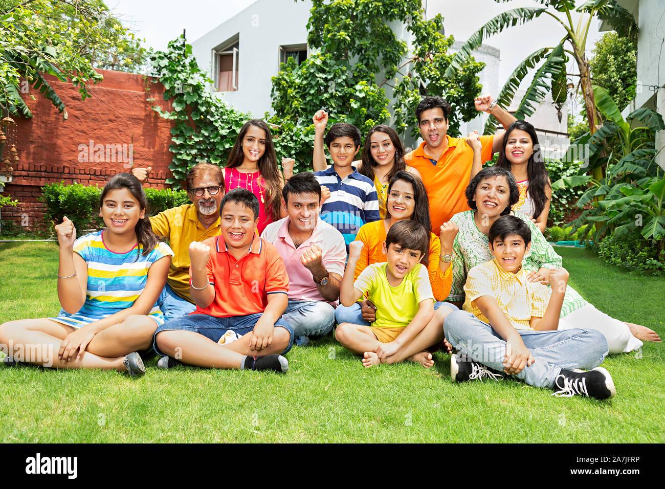 Gruppo di grandi famiglie i deputati seduti su erba insieme e Fists-Hand conquistando il successo celebrazione nel cortile di casa loro Foto Stock