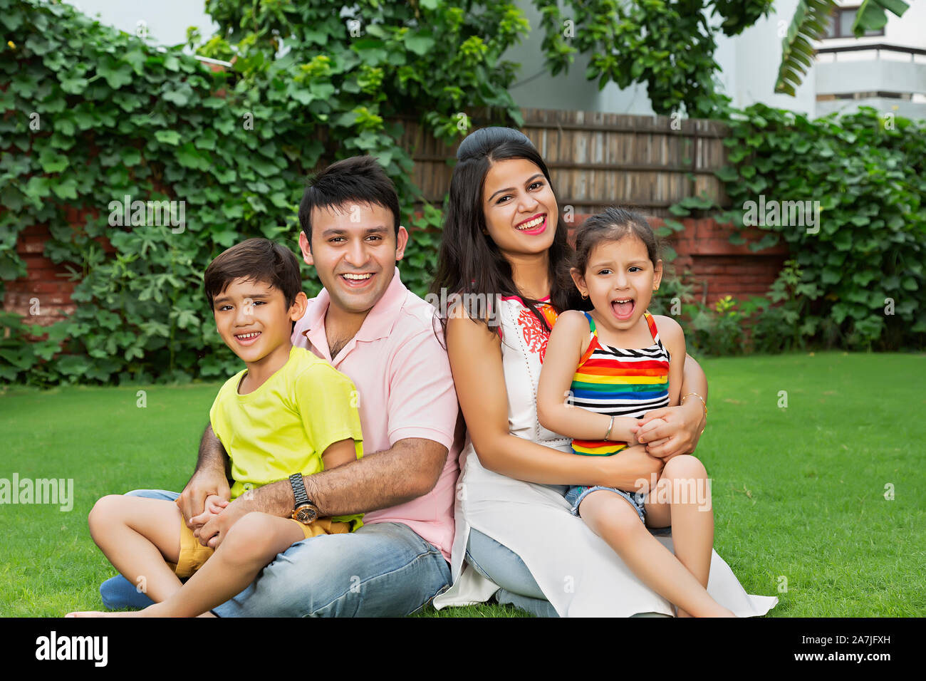 La famiglia felice i genitori e due bambini figlio ed figlia seduta su erba e rilassarsi nel cortile-di-la loro casa Foto Stock