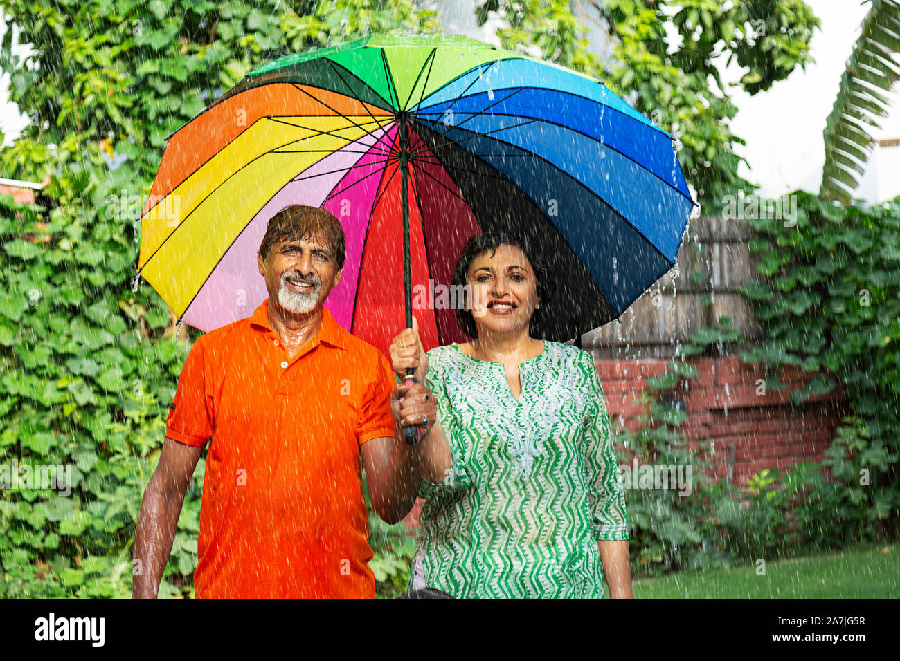Felice amorevole coppia di anziani sotto ombrello arcobaleno durante il piovoso in giardino Foto Stock