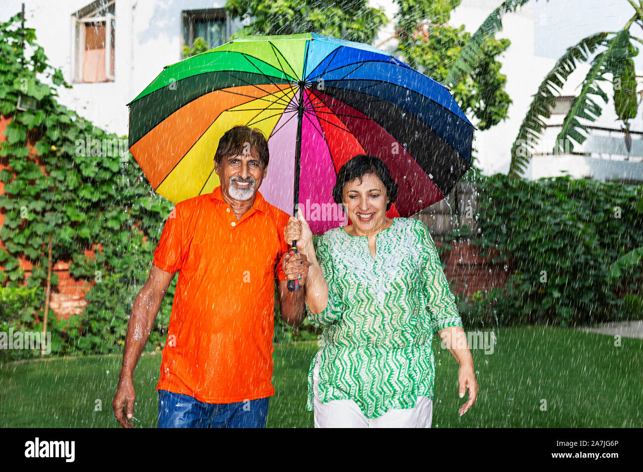 Felice Coppia di anziani sotto ombrellone a piedi godendo la pioggia in-park Foto Stock
