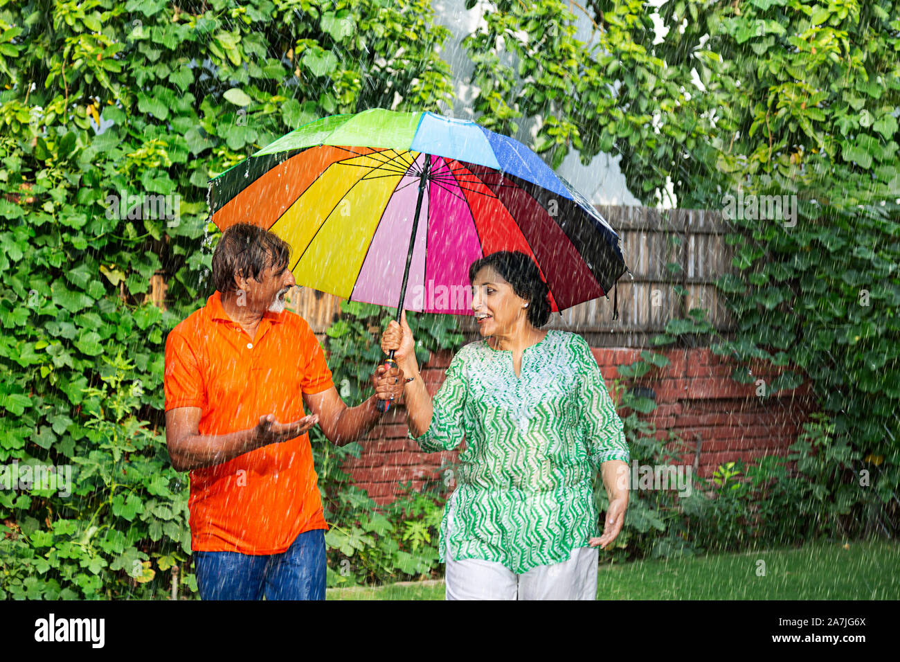 Felice amorevole coppia di anziani parlando sotto ombrello in caso di pioggia godendo di in-park Foto Stock