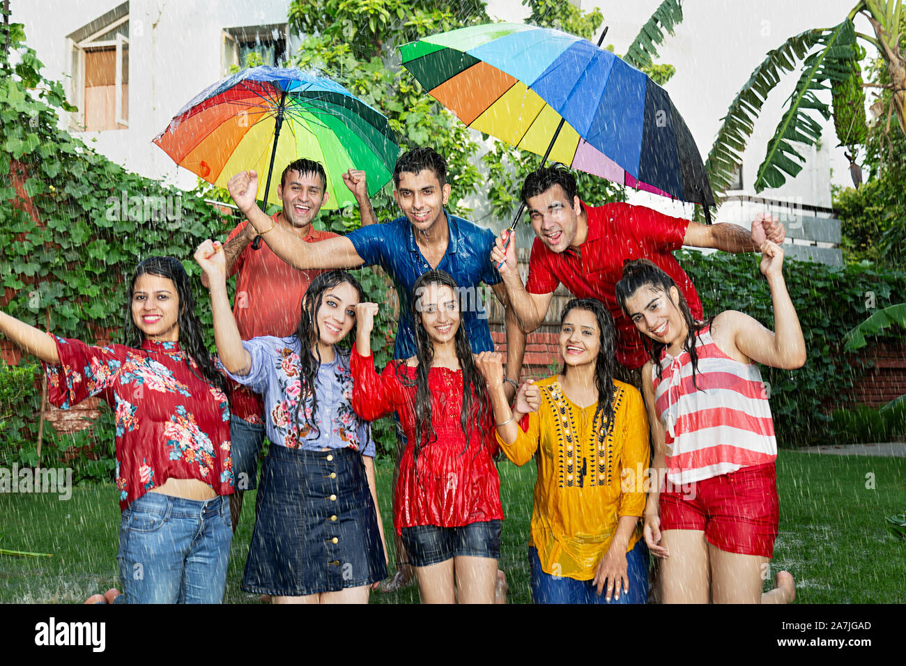 Group-Of adulto maschio e femmina di amici con ombrellone divertirsi godendosi la pioggia nel giardino di casa Foto Stock