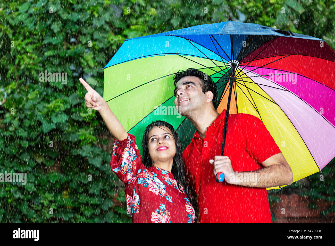 Sorridente coppia romantica sotto ombrellone rivolto lontano in giardino durante la pioggia pioggia Foto Stock