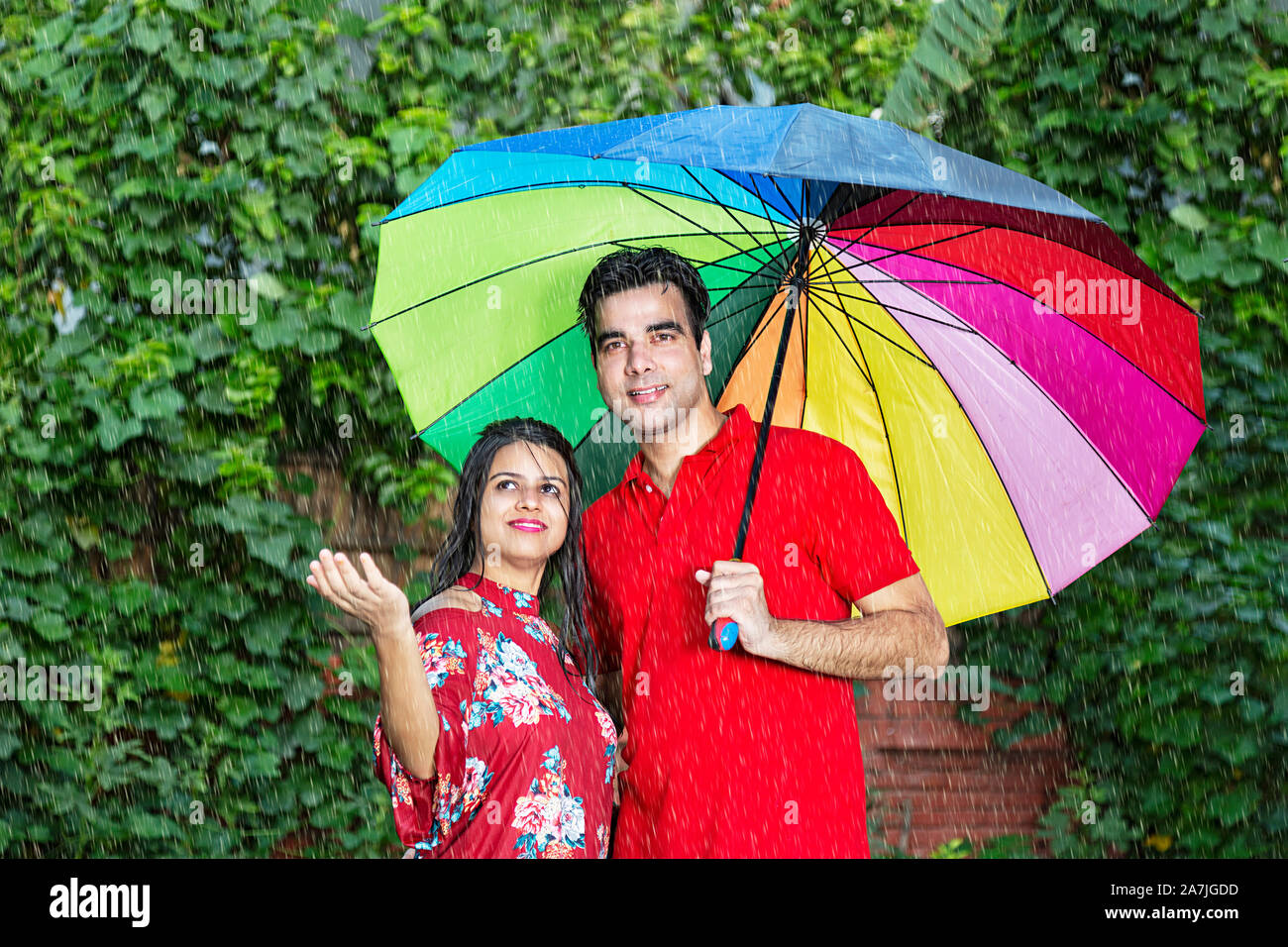 Romantica felice coppia sposata sotto ombrellone gustando sotto la pioggia in giardino esterno Foto Stock