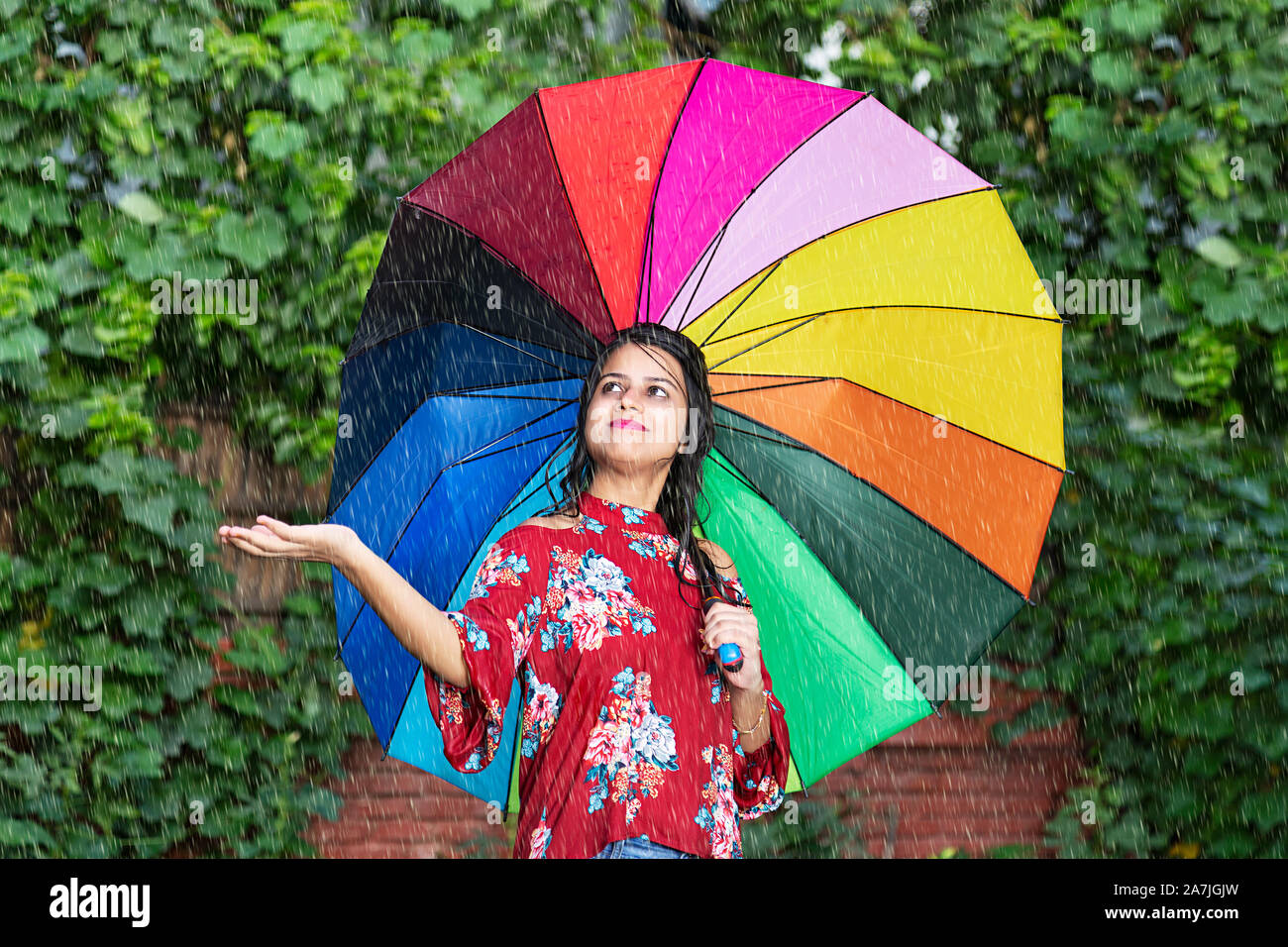 Sorridenti femmina adulta con ombrello sotto la pioggia battente in parco all'aperto Foto Stock