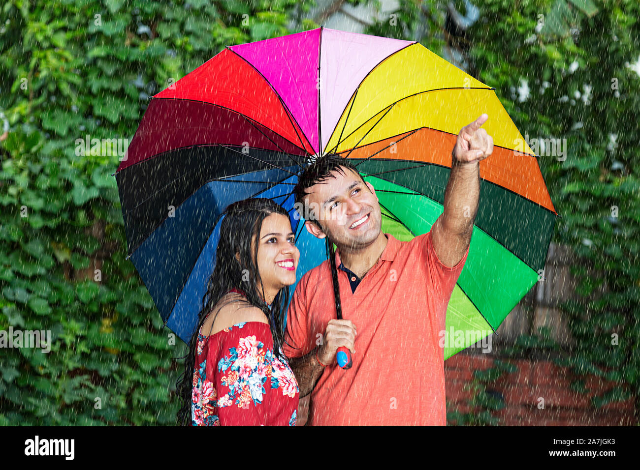 Felice di amare giovane sotto ombrellone puntato da qualche parte in-park durante la pioggia sulla stagione estiva Foto Stock