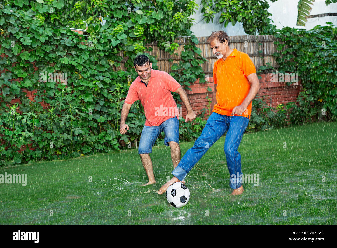 Adult-Son e invecchiato padre giocando a calcio In-The pioggia Of-Their In-Park House Foto Stock