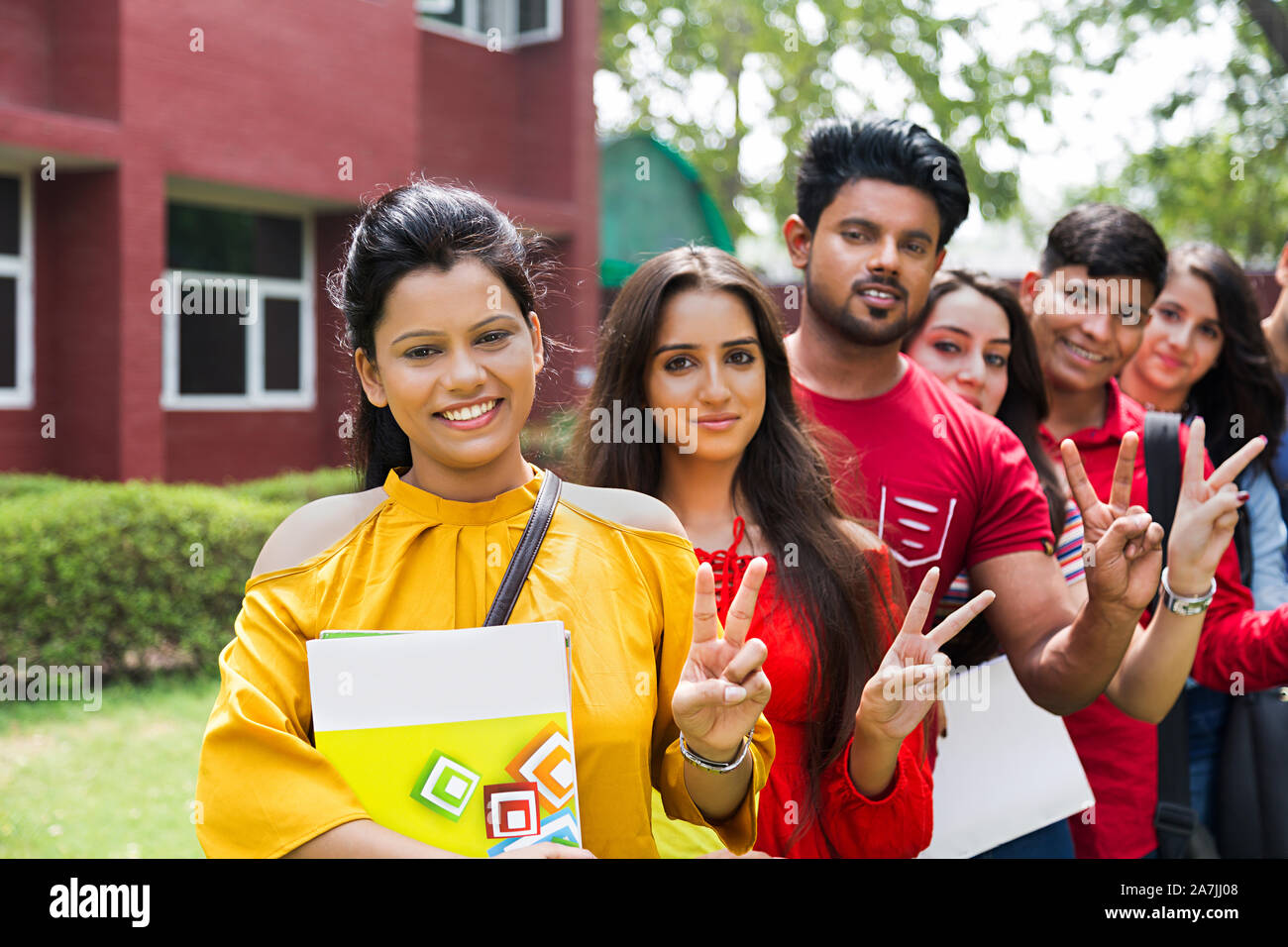 Un gruppo di giovani maschi e femmine studenti del college amici In-Queue permanente e rendendo V-Sign At-Campus Foto Stock