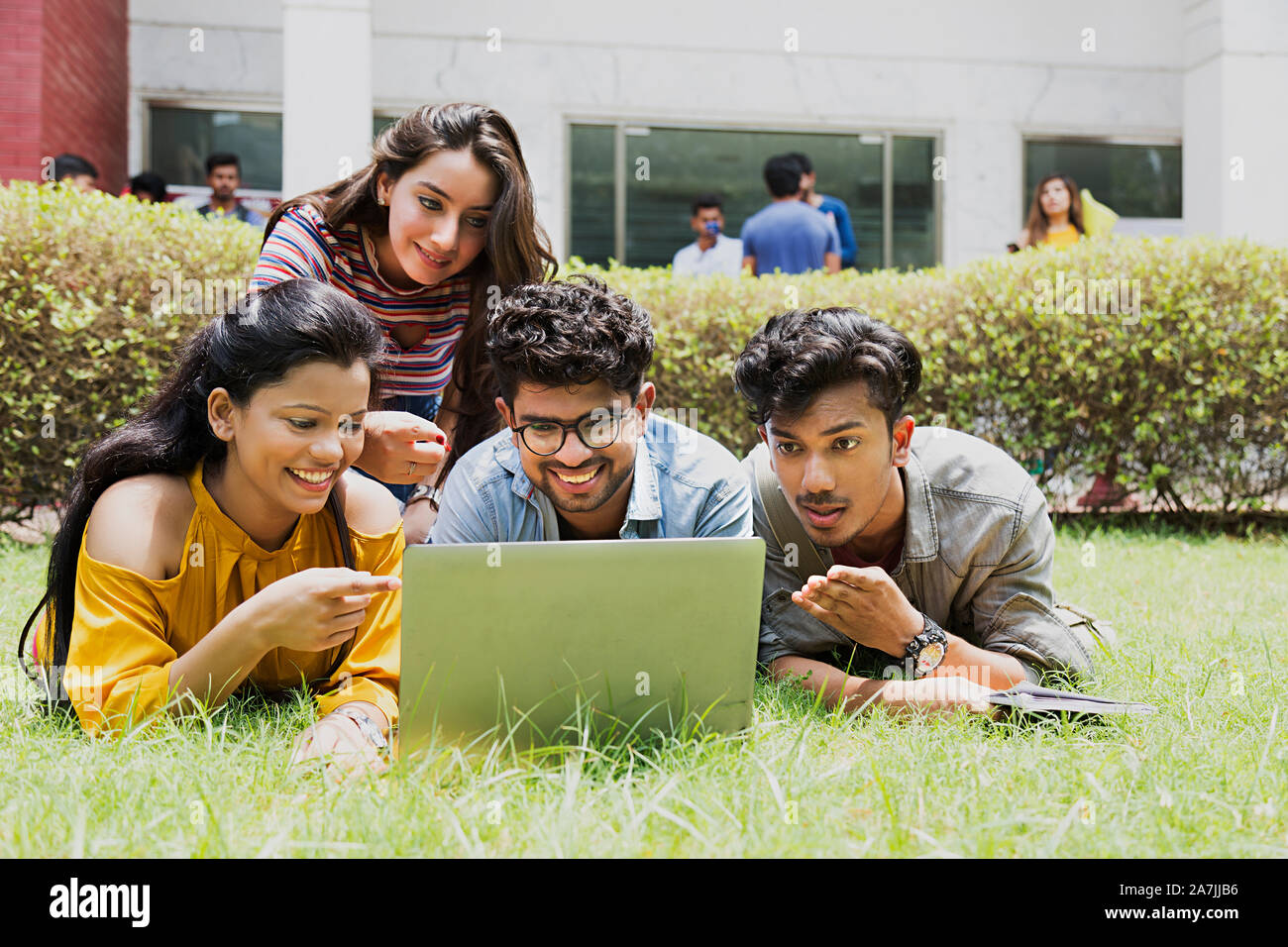 Collegio quattro ragazzi e ragazze studenti amici giacente su erba Looking-At-schermo portatile studiando In-Outside Campus Foto Stock