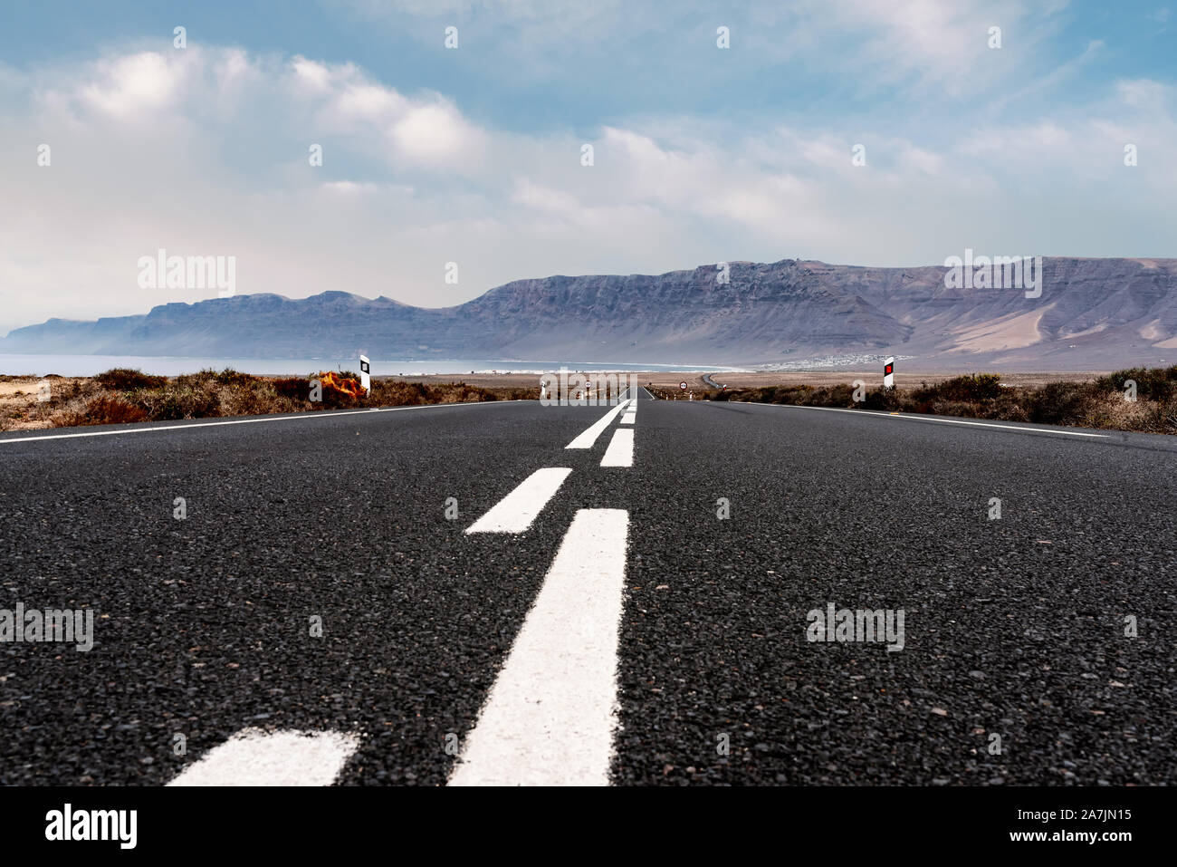 Lungo rettilineo vuoto strada asfaltata attraverso il paesaggio arido contro l'oceano e la gamma della montagna a Lanzarote isole Canarie Foto Stock