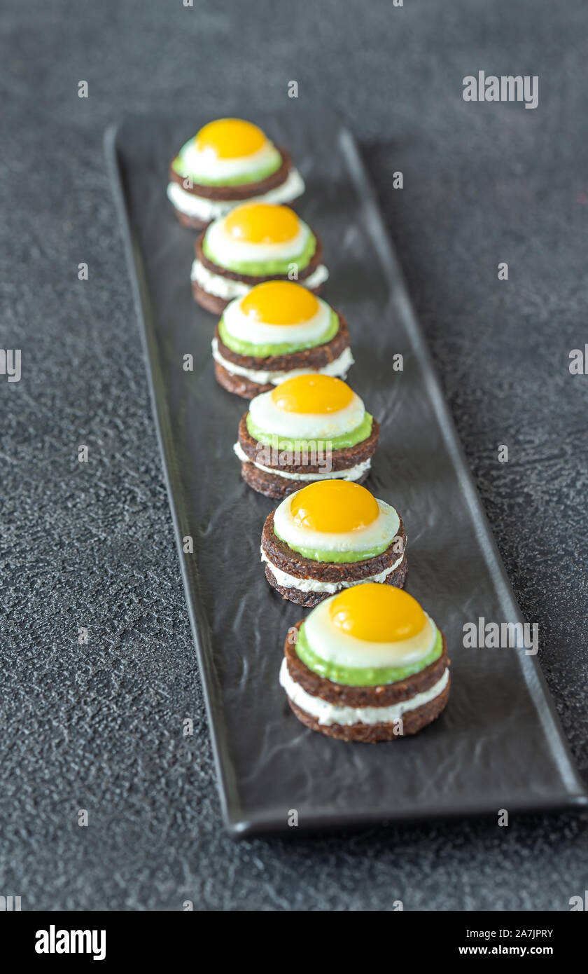 Crostino con crema di formaggio, guacamole fritte e uova di quaglia su piastra Foto Stock