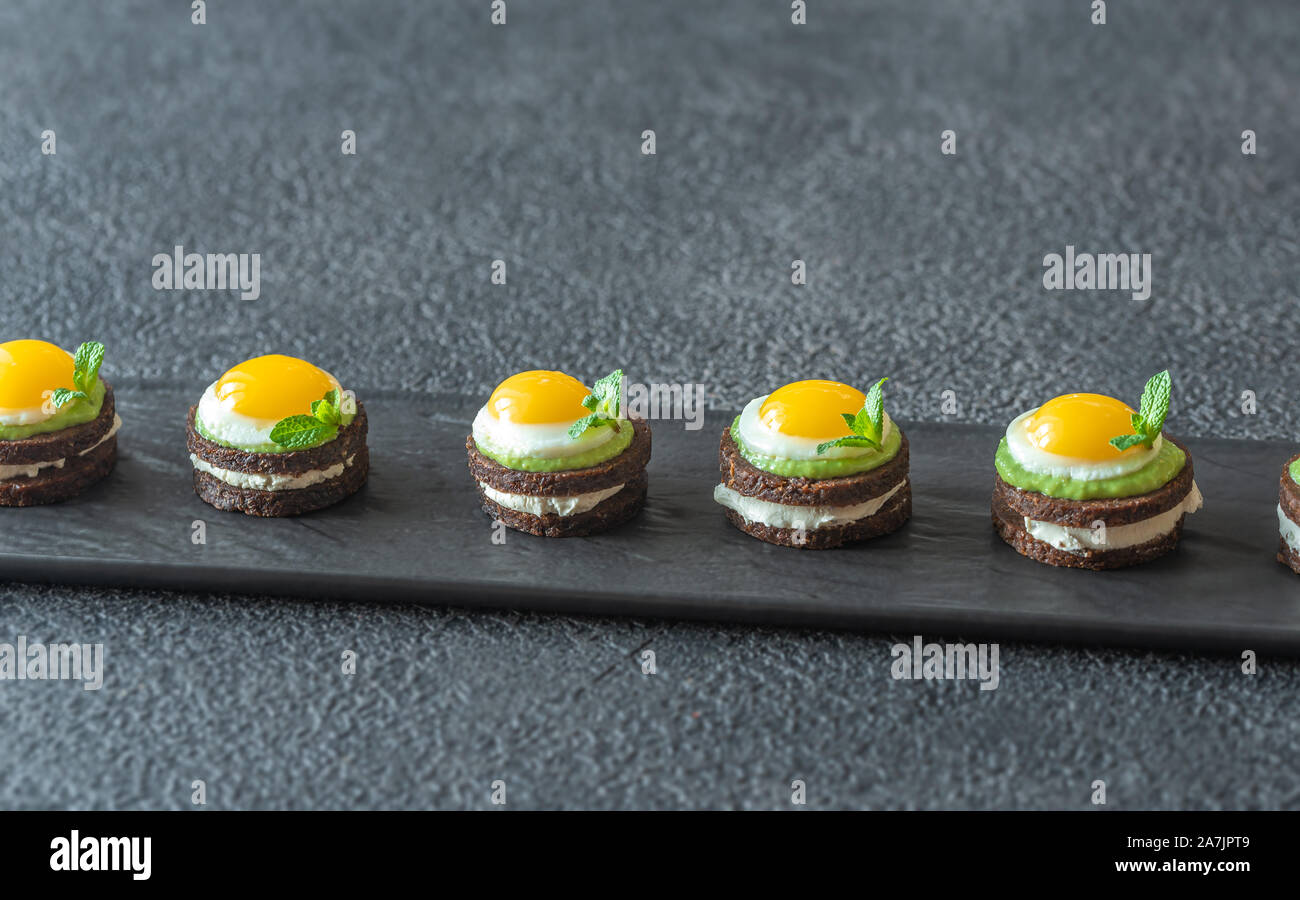 Crostino con crema di formaggio, guacamole fritte e uova di quaglia su piastra Foto Stock