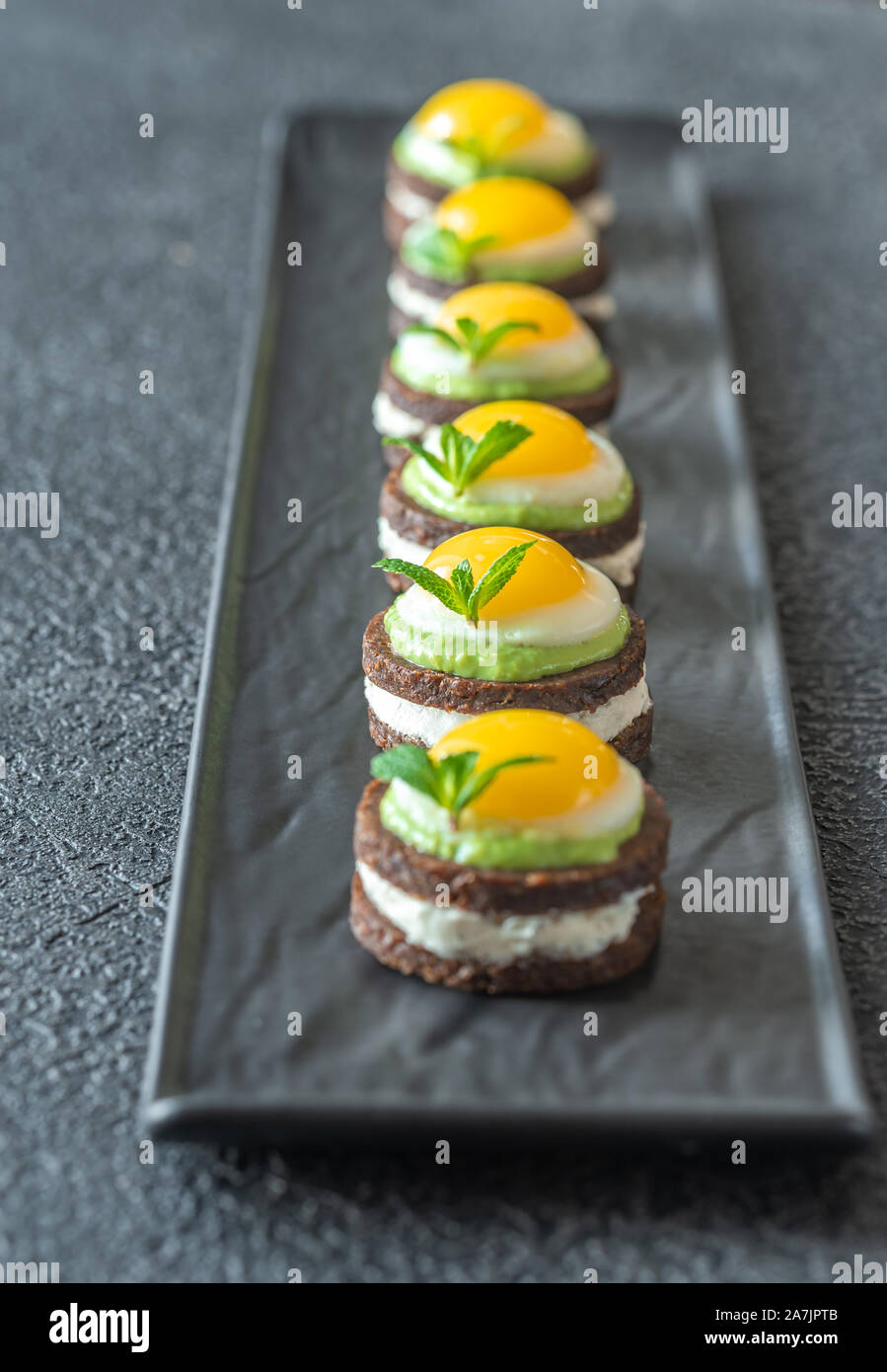 Crostino con crema di formaggio, guacamole fritte e uova di quaglia su piastra Foto Stock