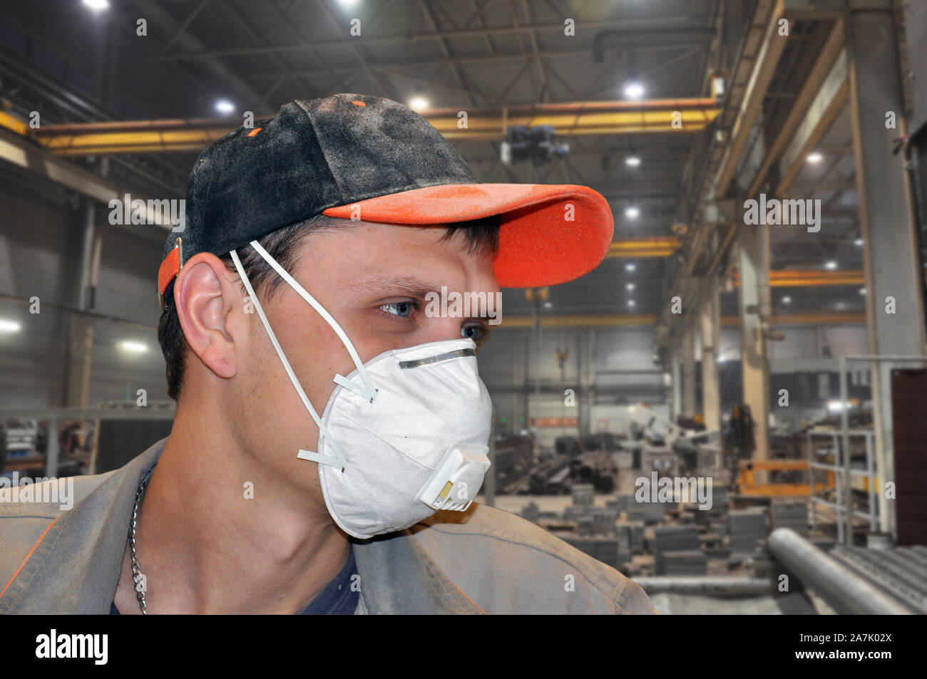 Giovane uomo in una maschera di protezione contro la polvere e polverosa cap a lavoro. Equipaggiamento protettivo personale Foto Stock