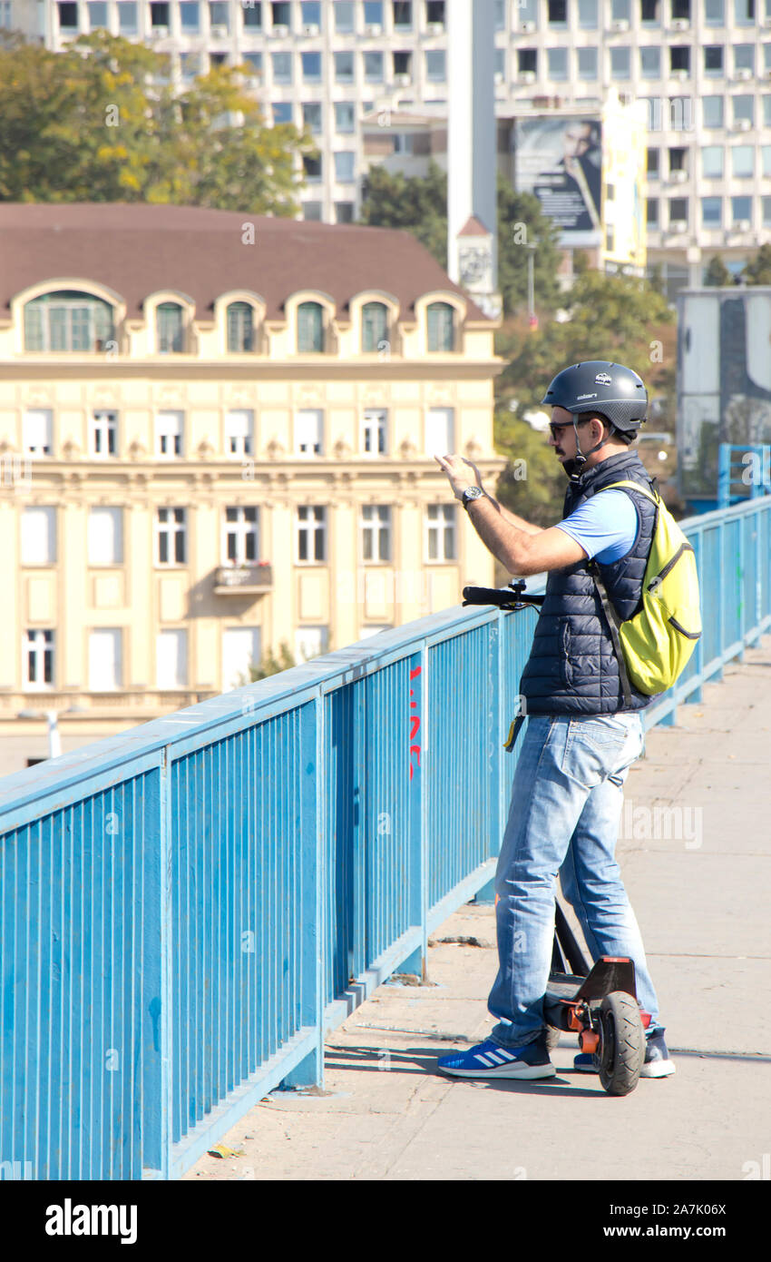A Belgrado, in Serbia - Ottobre 16, 2019: Un uomo turistico sightseeing mentre cavalcate un scooter elettrico sulla città street bridge marciapiede Foto Stock