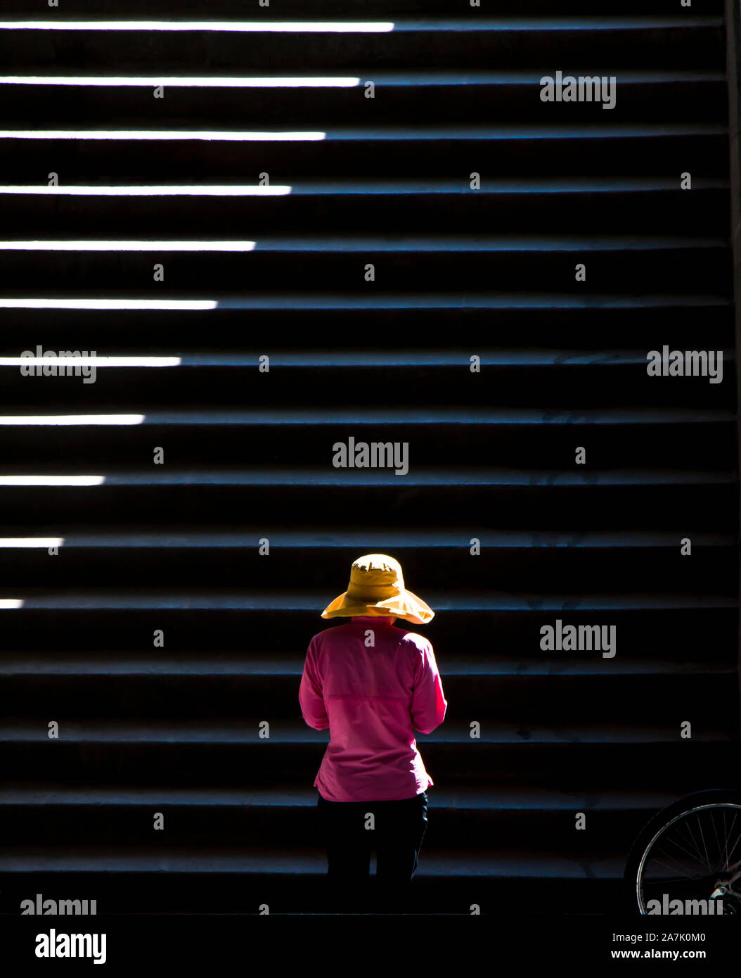 Una donna che indossa cappello giallo a piedi fino al pubblico le scale di luce e ombre, e una ruota di bicicletta dettaglio , su una vite senza fine giornata autunnale Foto Stock