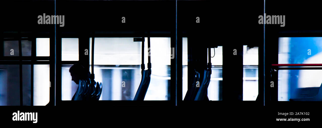 Uno sfocato persona seduta da soli all'interno del bus vuoti al posto di guida durante la notte, l'ultimo passeggero, attraverso Windows dall'esterno Foto Stock