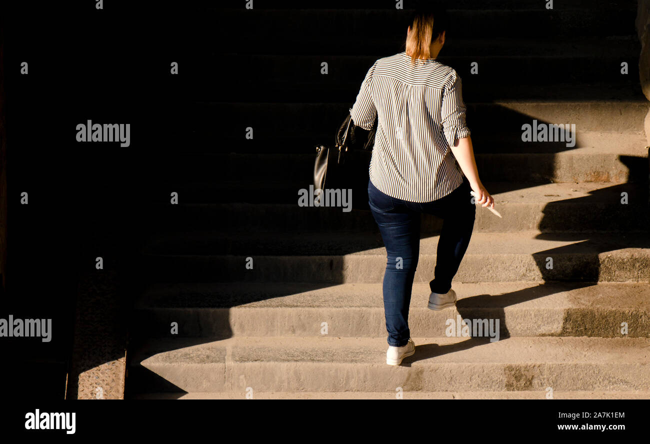 Uno più dimensione donna a piedi fino al pubblico le scale di luce e ombre, da dietro Foto Stock