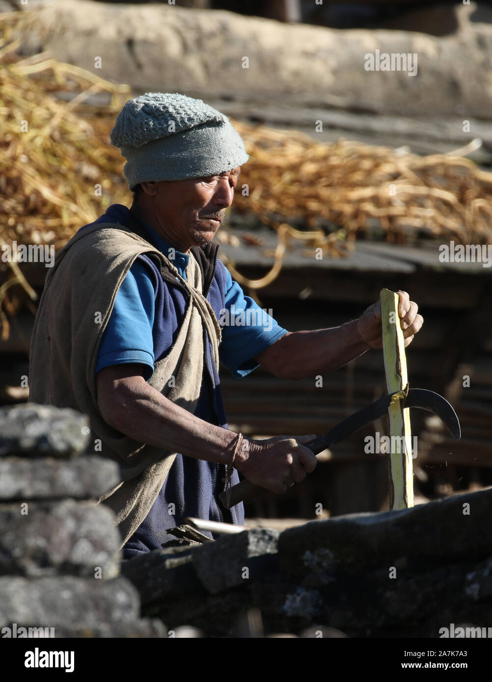 Un uomo Gurung indossando abiti tradizionali braciole di un pezzo di legno con un utensile tradizionale. Sikles, Himalaya, Nepal. Foto Stock