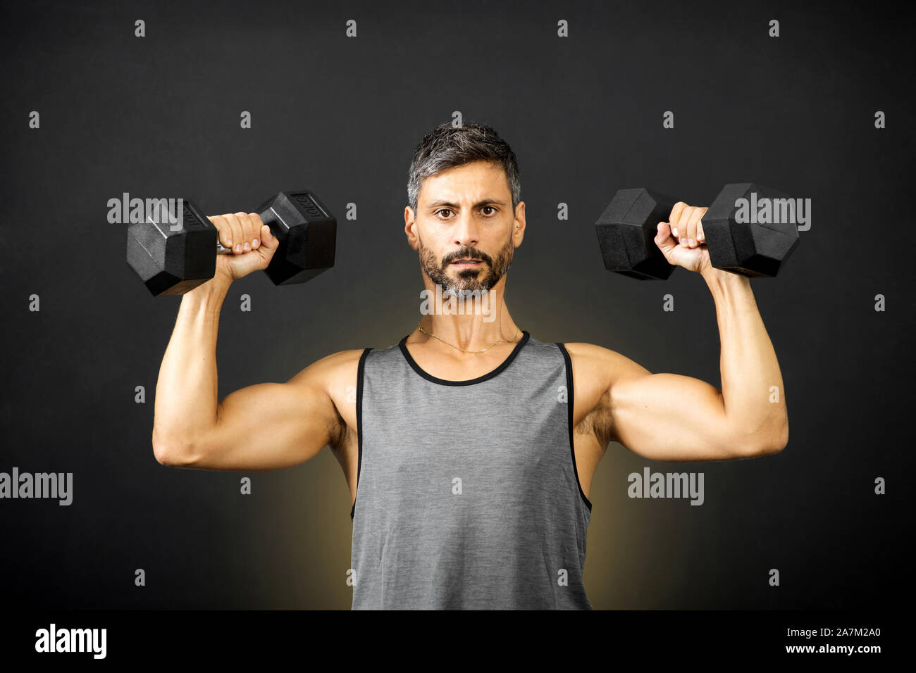Montare l'uomo muscolare il sollevamento pesi con manubri in una palestra bodybuilding facendo esercizi per rafforzare i suoi muscoli in una salute e concetto di fitness Foto Stock