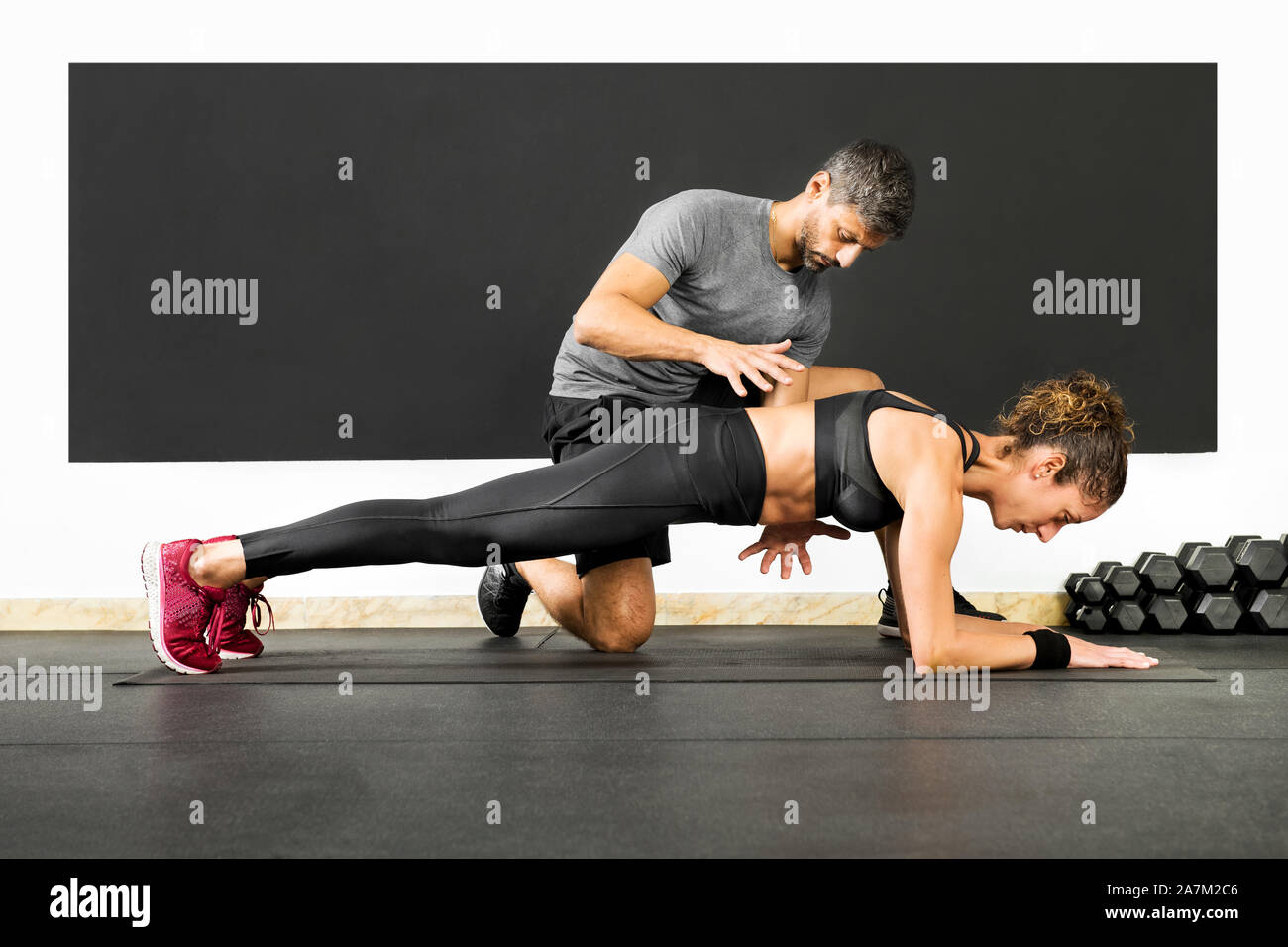 Donna in palestra facendo plank esercizio con l'aiuto di un professionista personal trainer, visto dal lato dal livello del pavimento Foto Stock