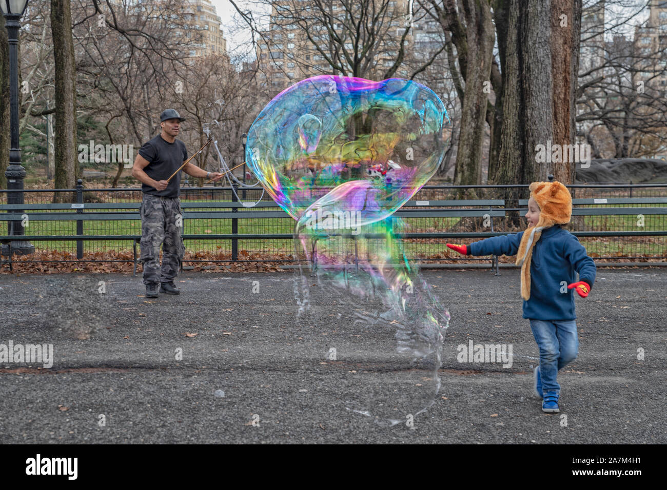 New York, STATI UNITI D'AMERICA-dicembre 17,2018: un uomo soffia bolle grandi nel Central Park di New York con un bellissimo bambino contento di toccarlo prima che rompe il giorno Foto Stock