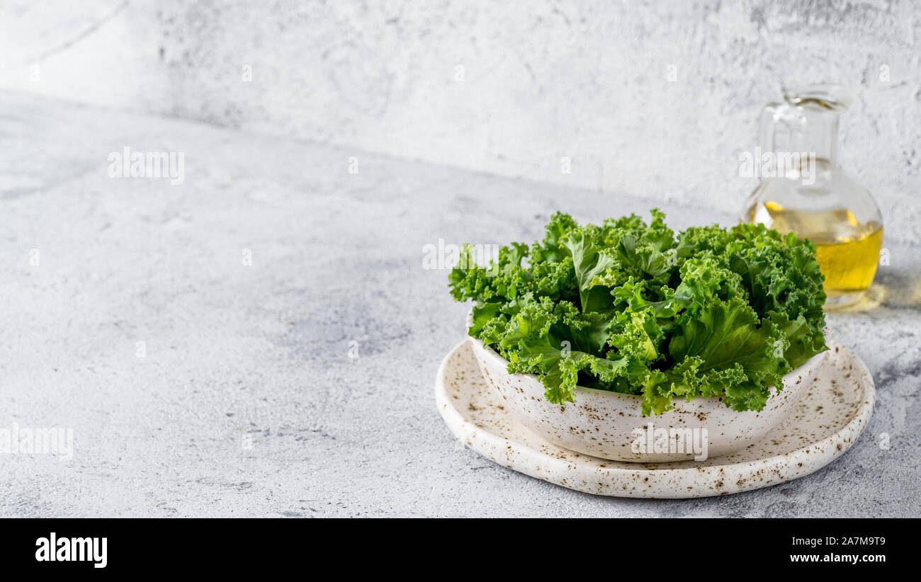 Verde foglie di cavolo bianco craft ciotola sul cemento grigio Sfondo. Mangiare sano, cibo vegetariano, dieta concetto. Copia spazio a sinistra. Salute kale benefici. Banner Foto Stock