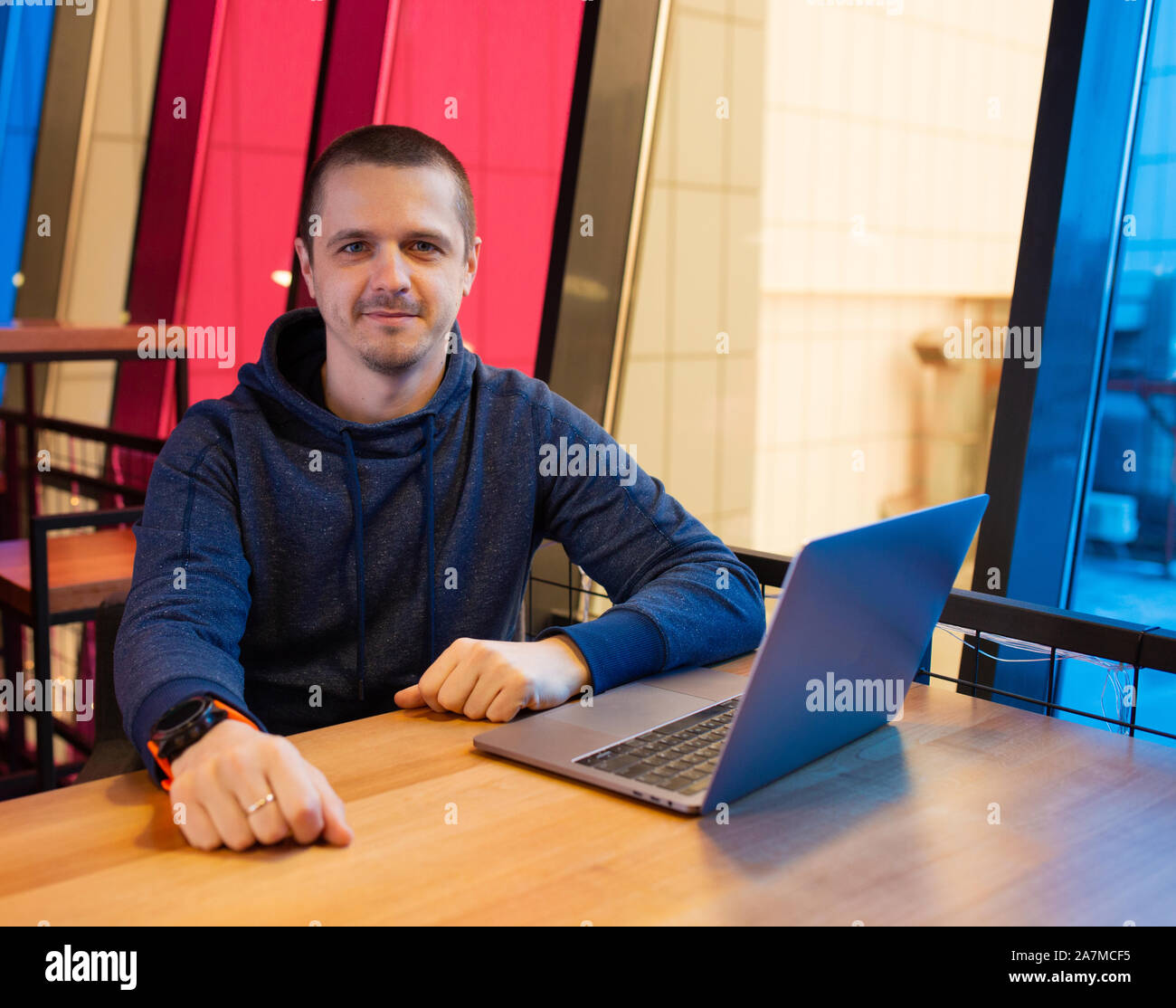Uomo in felpa con cappuccio seduti alla scrivania con computer portatile Foto Stock
