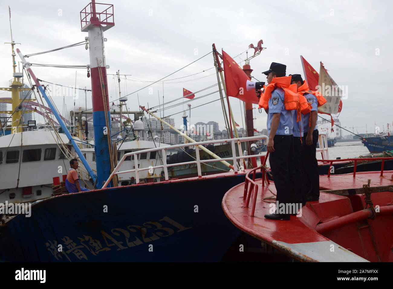 Poliziotti di aiutare i pescatori locali per rafforzare le barche dei pescatori e a prepararsi per la prossima Typhoon Mitag in Zhoushan city, est della Cina di provincia dello Zhejiang Foto Stock