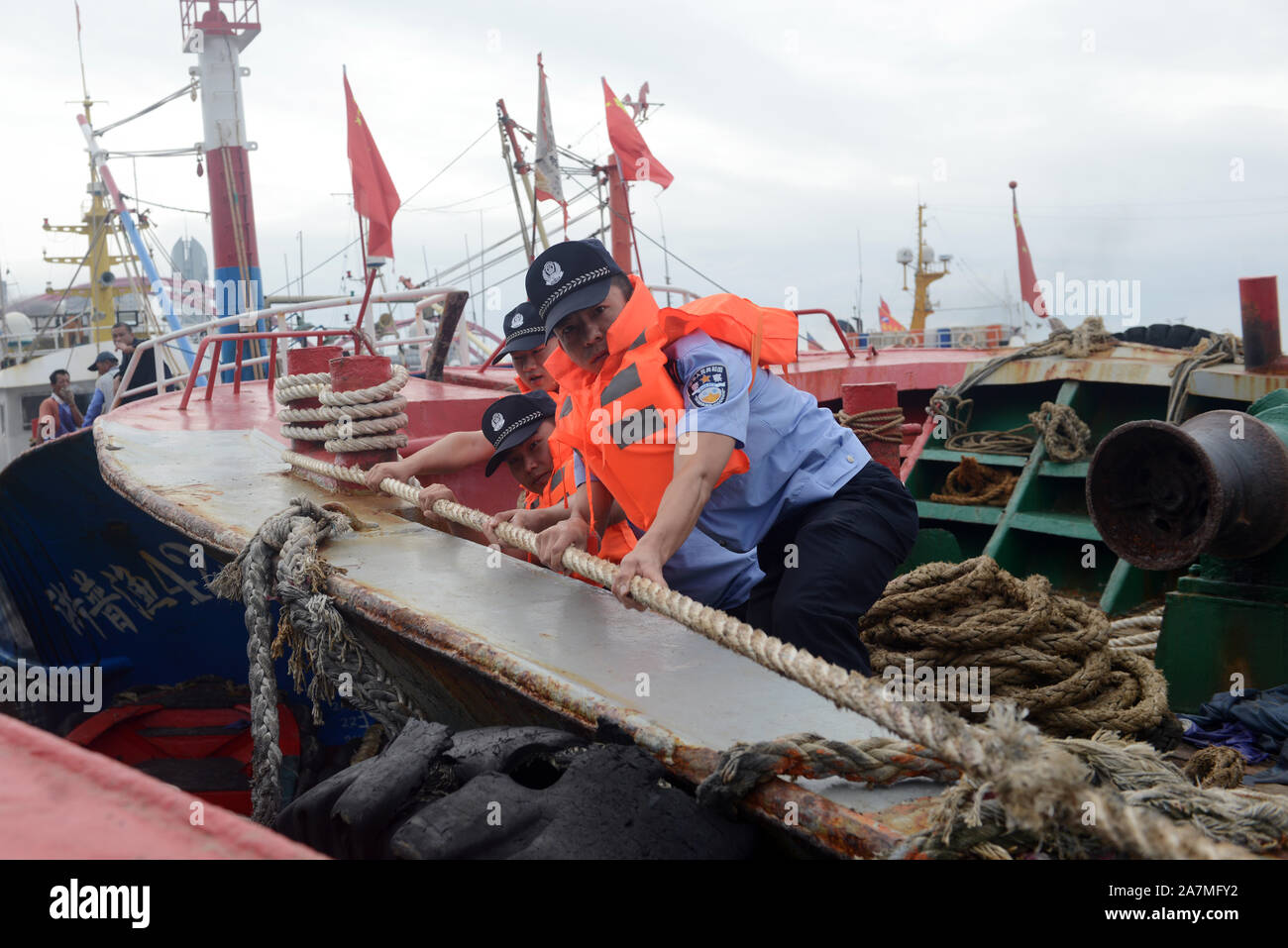 Poliziotti di aiutare i pescatori locali per rafforzare le barche dei pescatori e a prepararsi per la prossima Typhoon Mitag in Zhoushan city, est della Cina di provincia dello Zhejiang Foto Stock