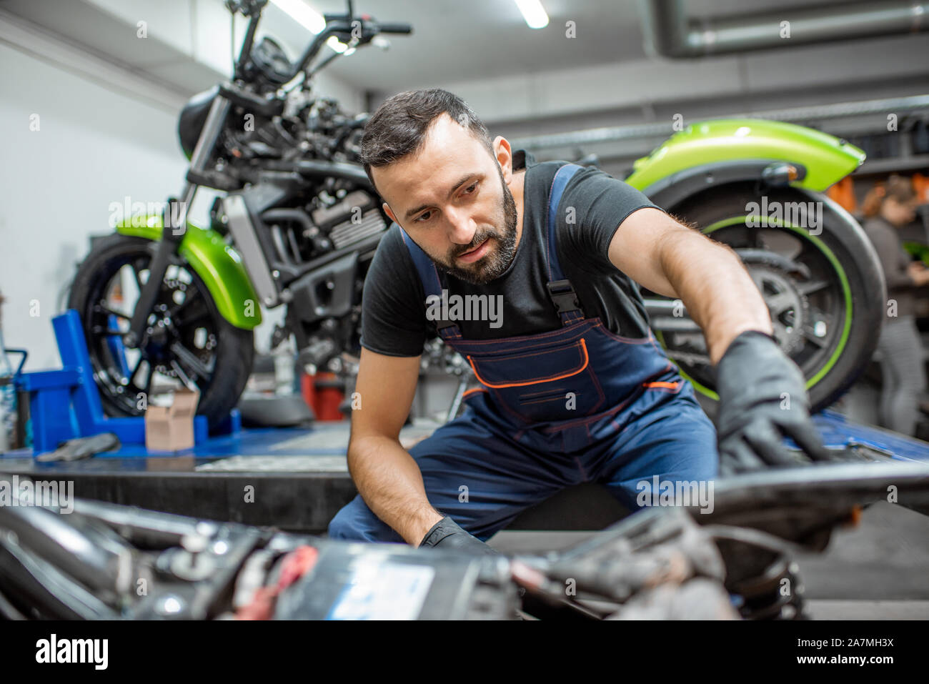 Ritratto di un bel barbuto biker in tute da lavoro seduta vicino alla moto durante la riparazione in officina Foto Stock