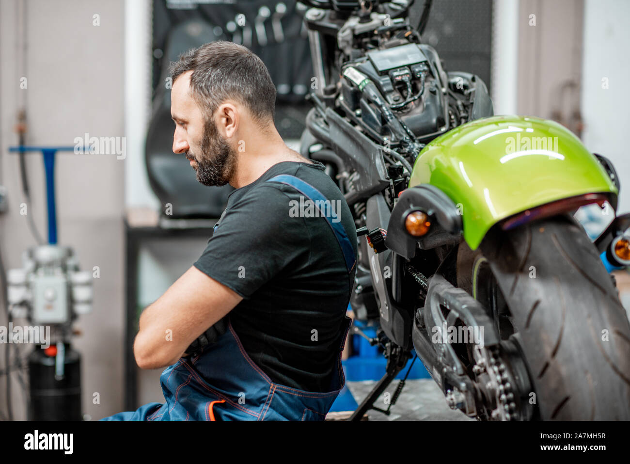 Ritratto di un bel barbuto biker in tute da lavoro seduta vicino alla moto durante la riparazione in officina Foto Stock