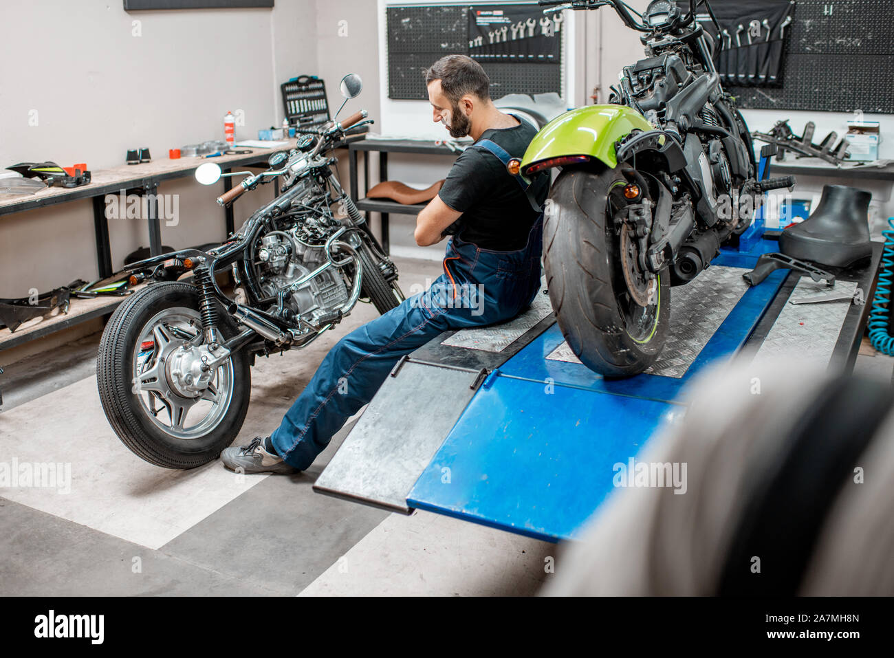 Ritratto di un bel barbuto biker in tute da lavoro seduta vicino alla moto durante la riparazione in officina Foto Stock