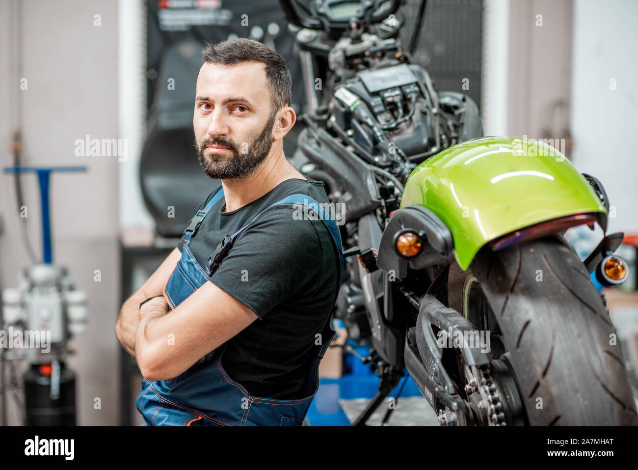 Ritratto di un bel barbuto biker in tute da lavoro seduta vicino alla moto durante la riparazione in officina Foto Stock