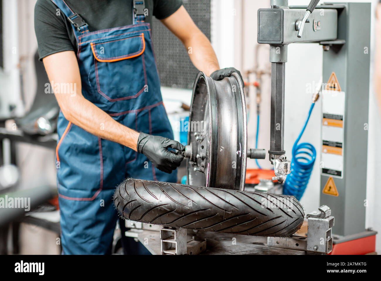 Lavoratore di servizio cambio pneumatici moto su un equipaggiamento speciale per l'installazione di pneumatici in officina, close-up con nessun volto Foto Stock