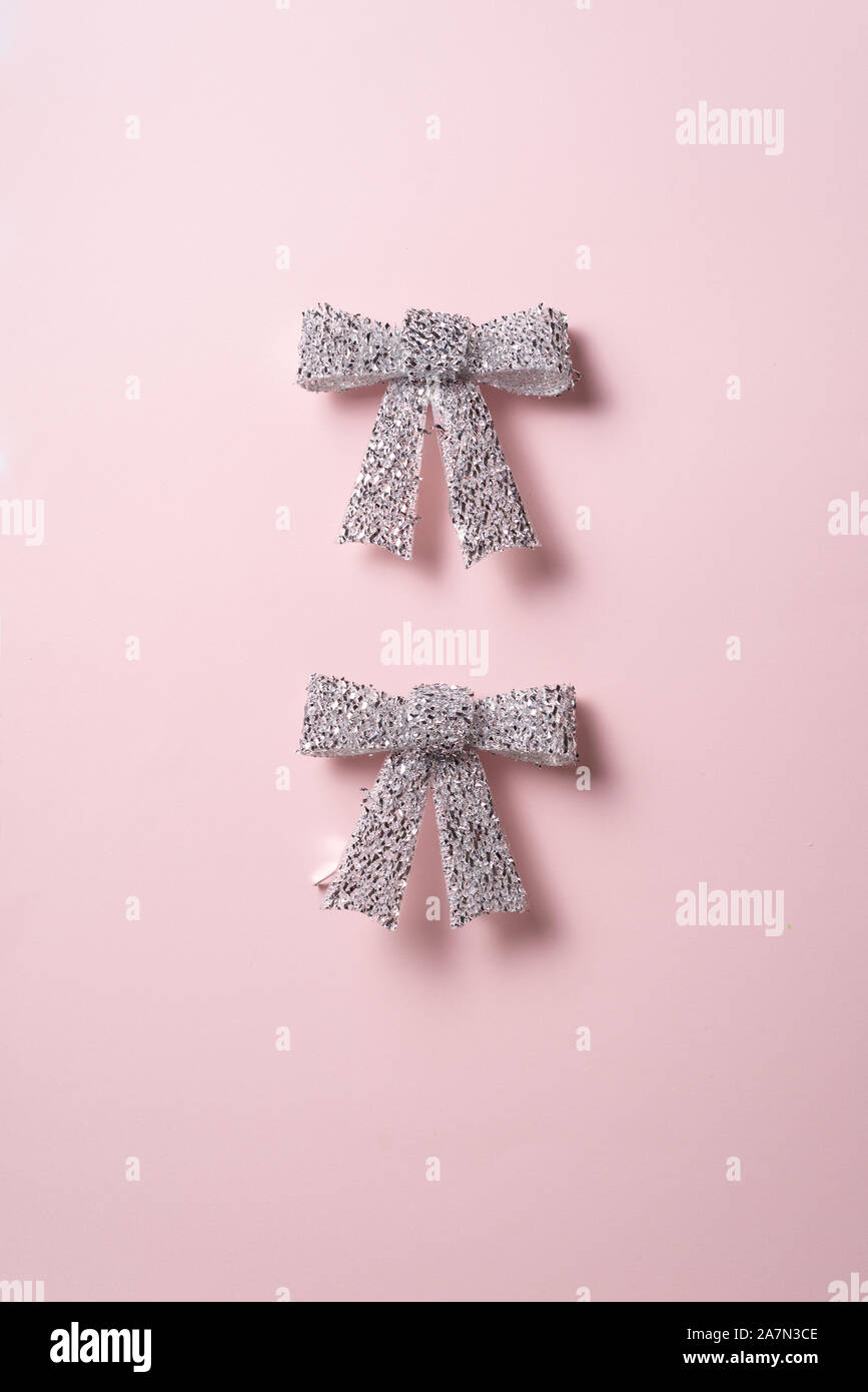 Holiday Decori Collezione,due Shiny Silver Ribbon bow su sfondo rosa. concetto per Natale e le vacanze. Foto Stock