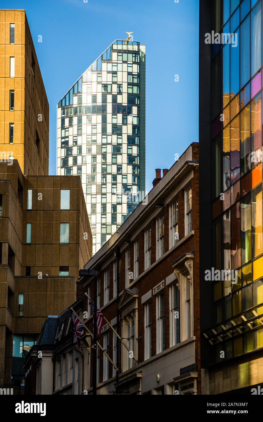 Una torre snella rivestita di vetro – forse la torre Beetham di 90 metri (West Tower), costruita nel 2004 – si erge tra edifici più antichi in mattoni e arenaria e una facciata con vetrate colorate nel centro di Liverpool, Inghilterra; due bandiere sventolano su uno degli edifici in primo piano. Foto Stock