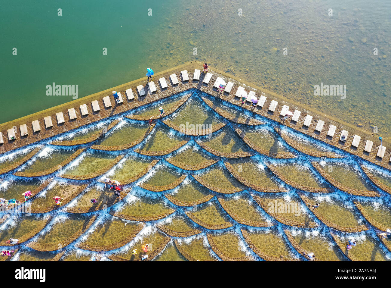 I visitatori un tuffo per rinfrescarsi in acqua in una posizione nota per il pesce in scala barriere sagomati che formano piccole cascate nel quartiere Fuyang, Hangzhou ci Foto Stock